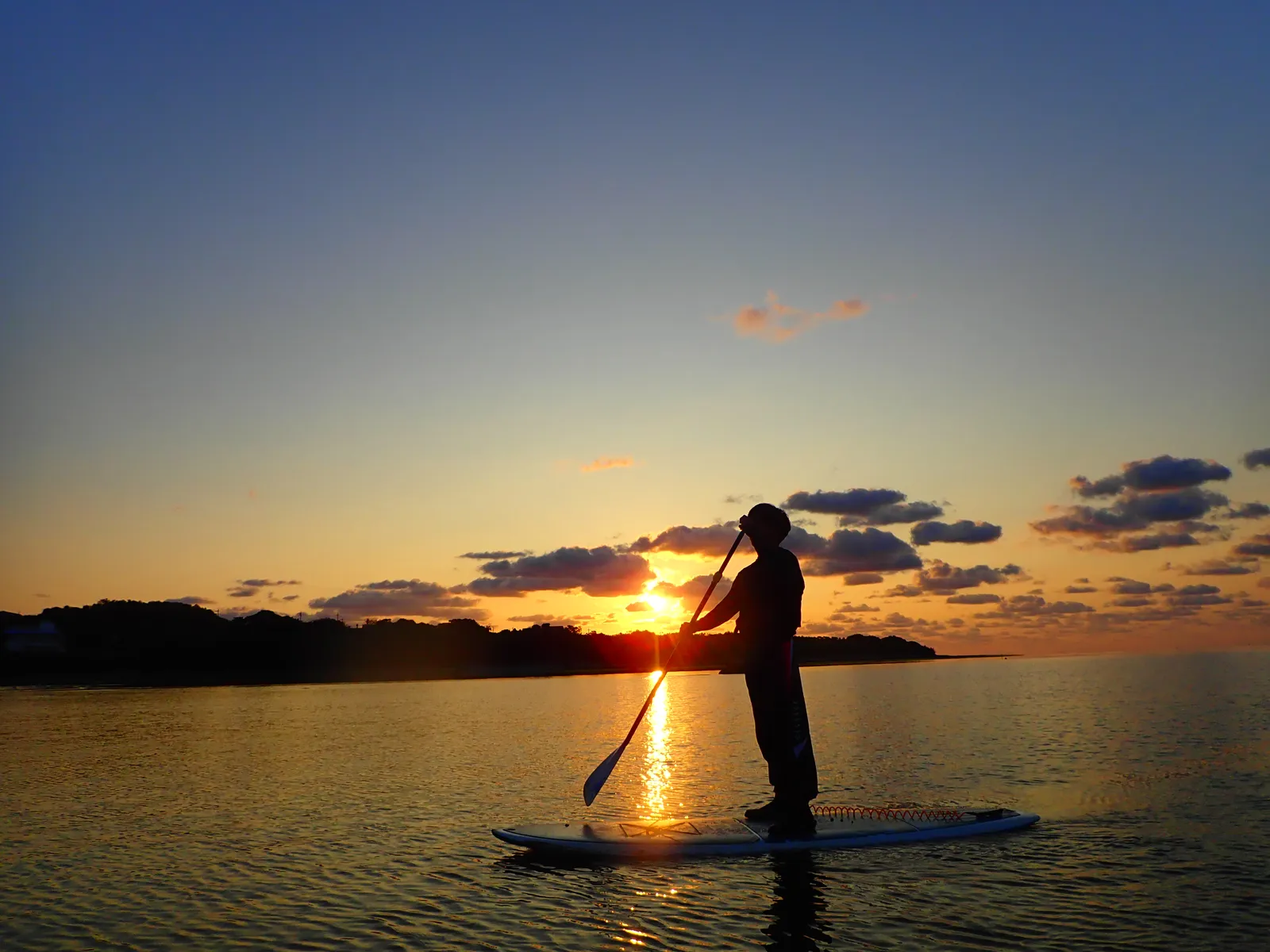 Silhouette of a person paddling a SUP with the rising sun behind