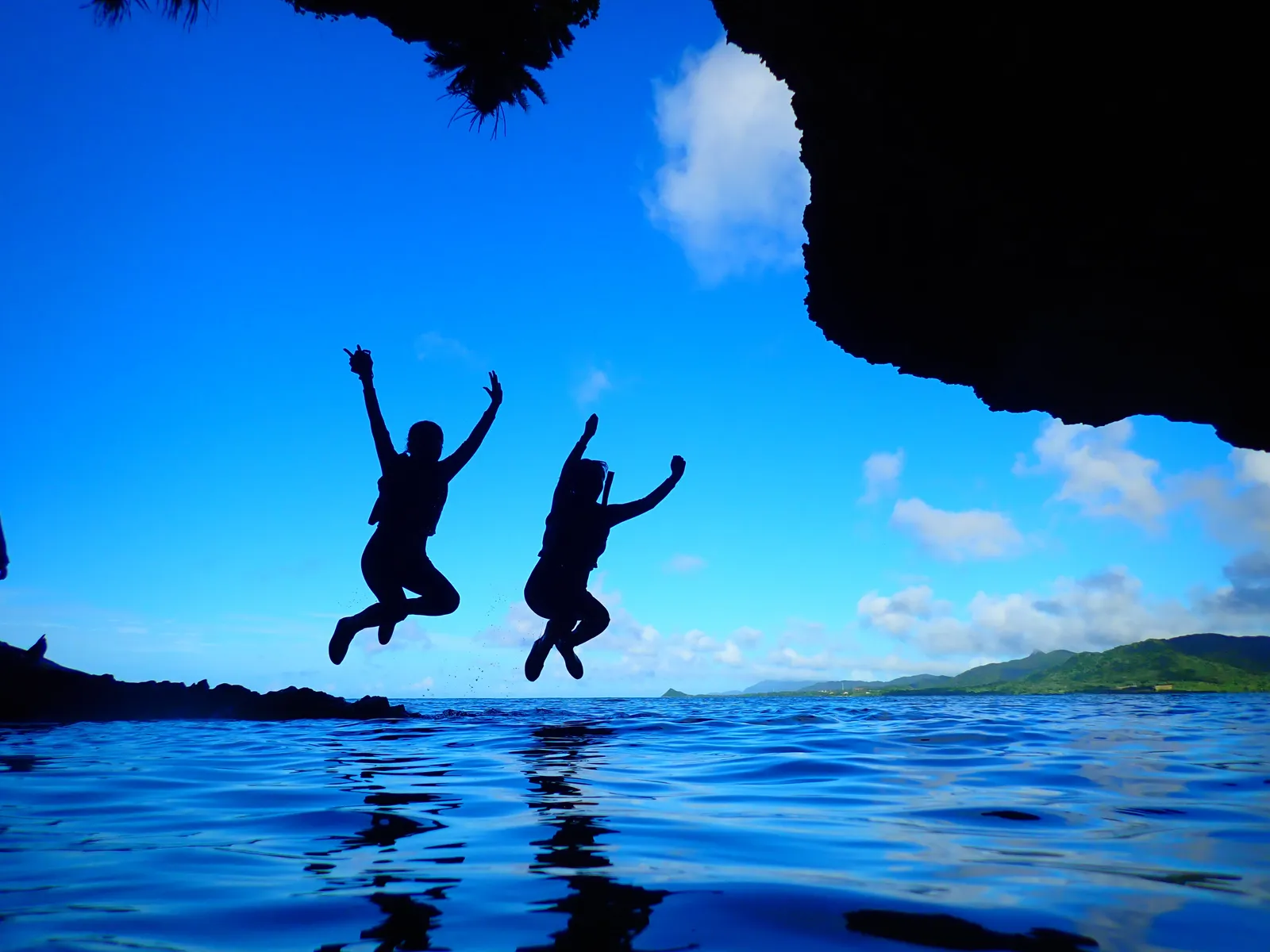Silhouettes of two people jumping with their arms raised, and their reflections on the sea