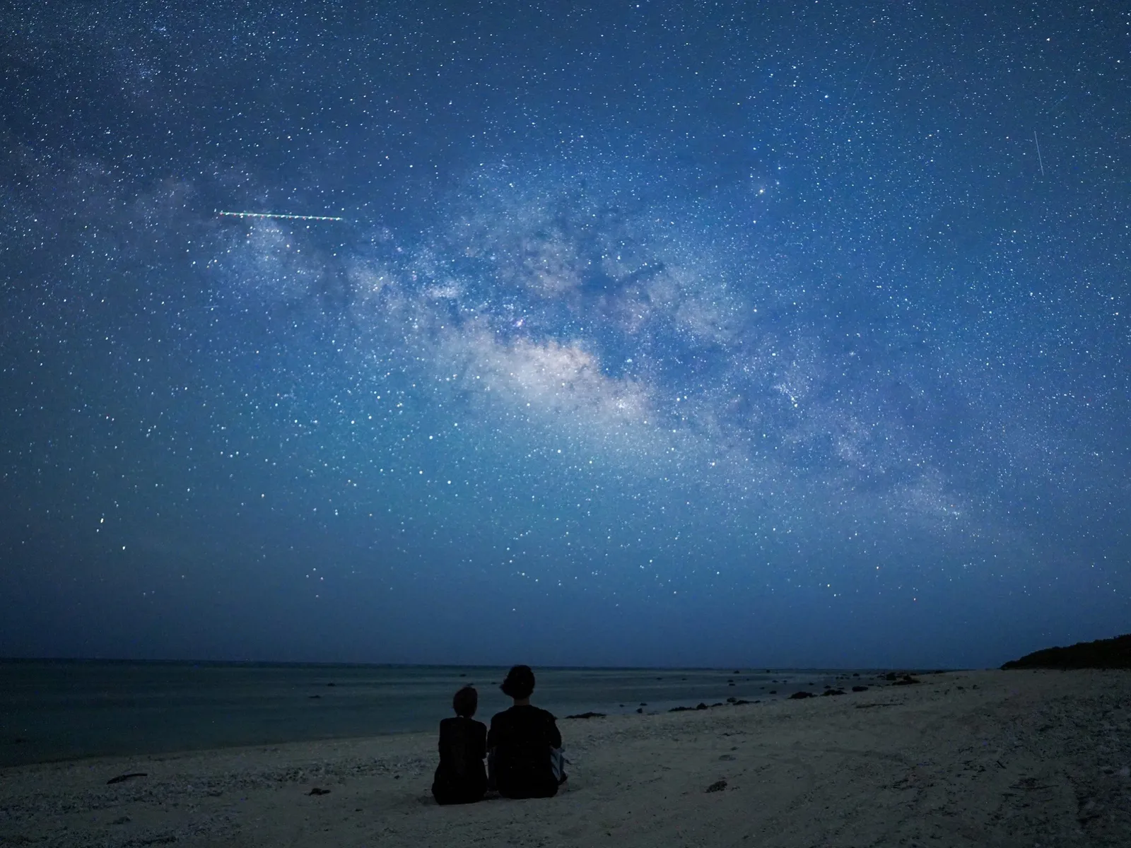 星空の下で砂浜に座る2人のシルエット
