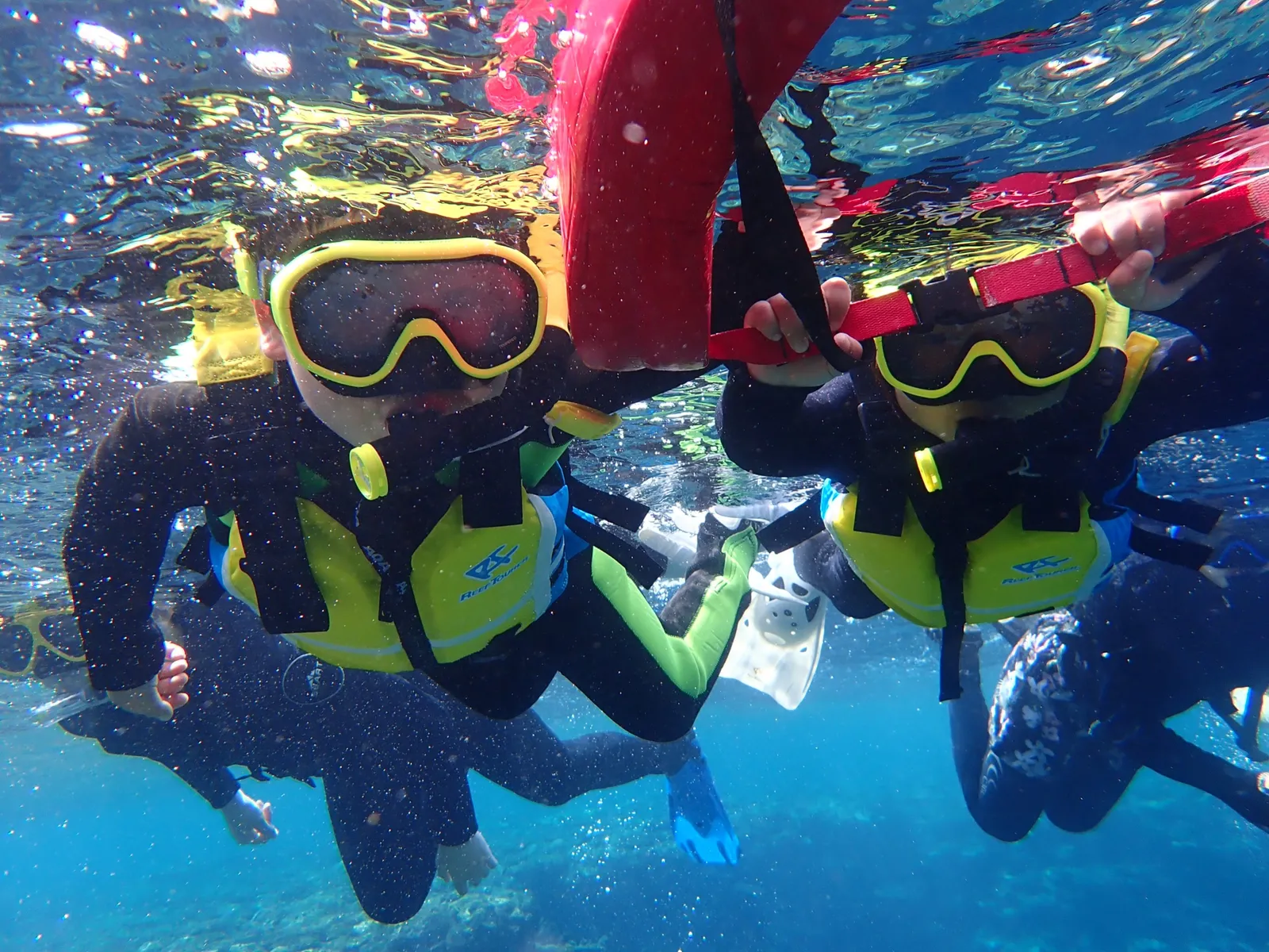 Children wearing masks and life jackets, swimming while holding onto flotation devices