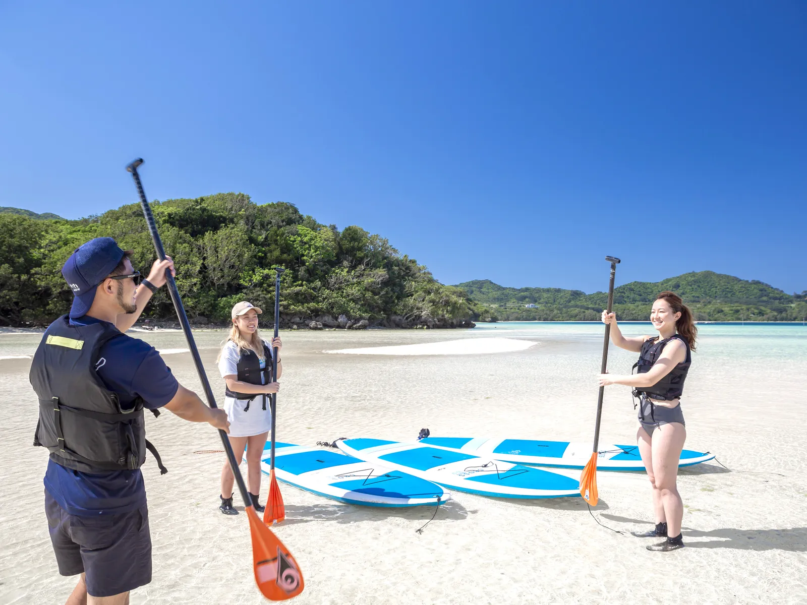 A guide and two participants holding paddles on the beach, with SUP boards lined up