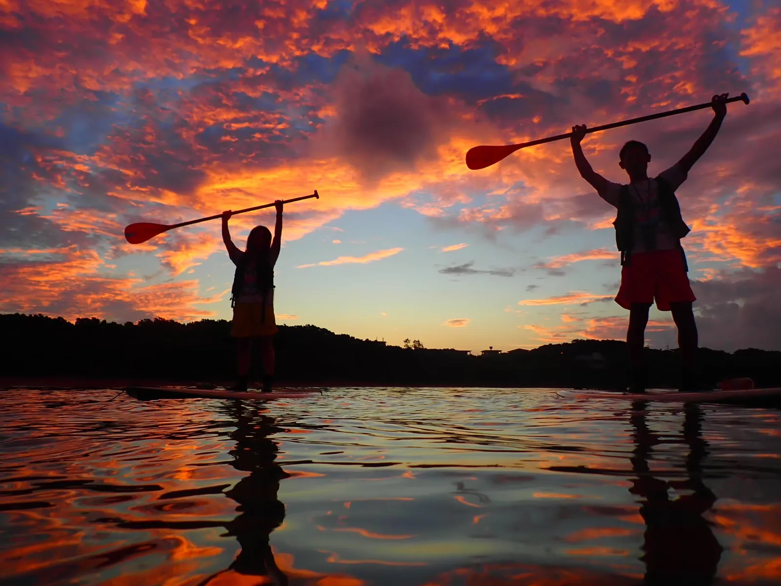 Two people raising their paddles under a blazing red dawn sky