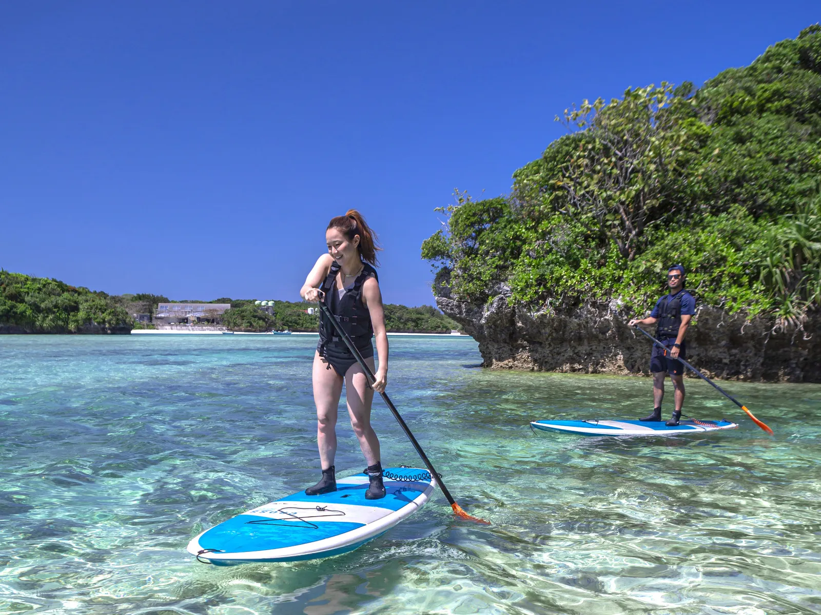 A woman and a guide standing on SUP boards near a rocky outcrop