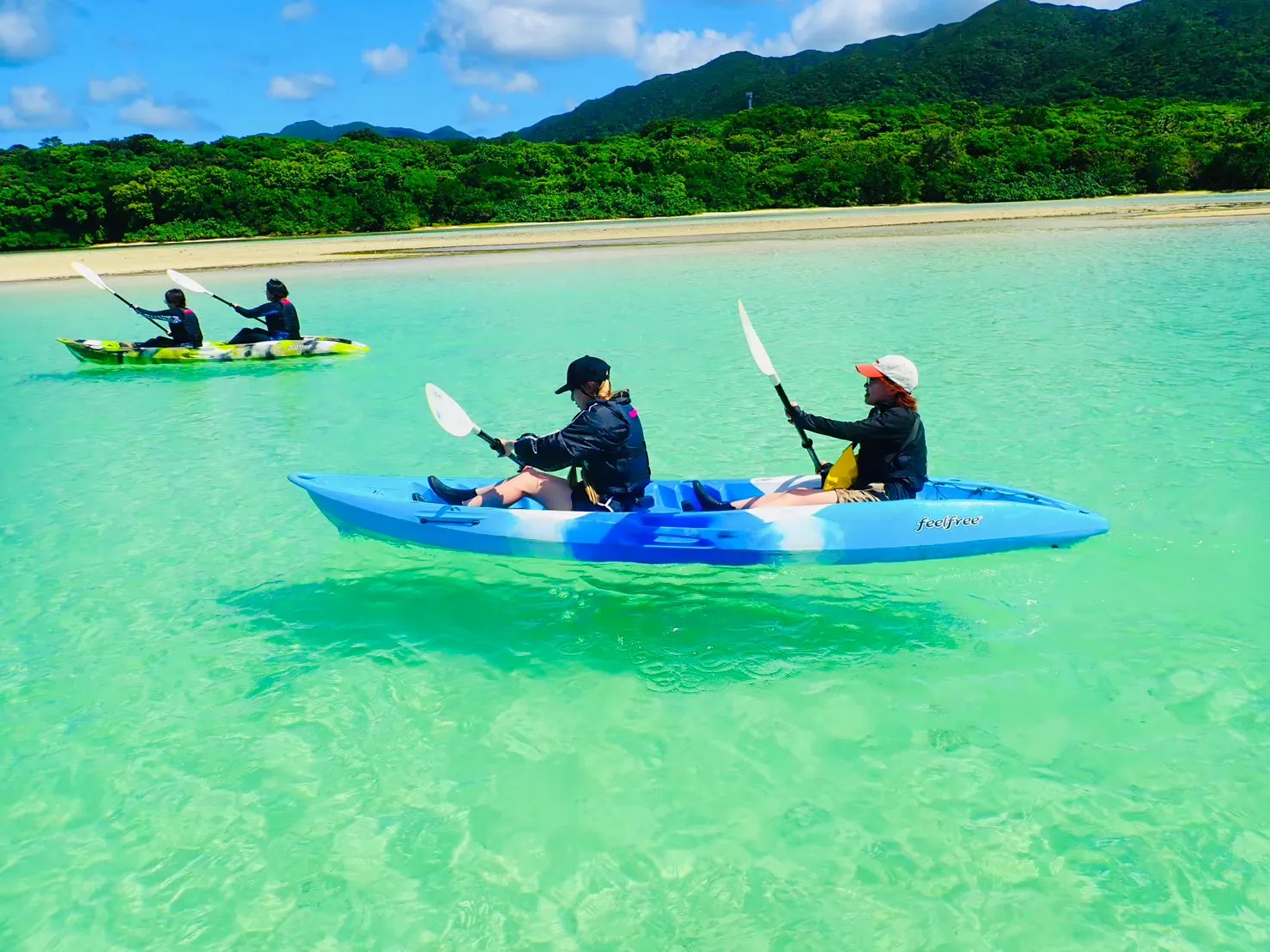Two canoes gliding across emerald-green water with green mountains behind
