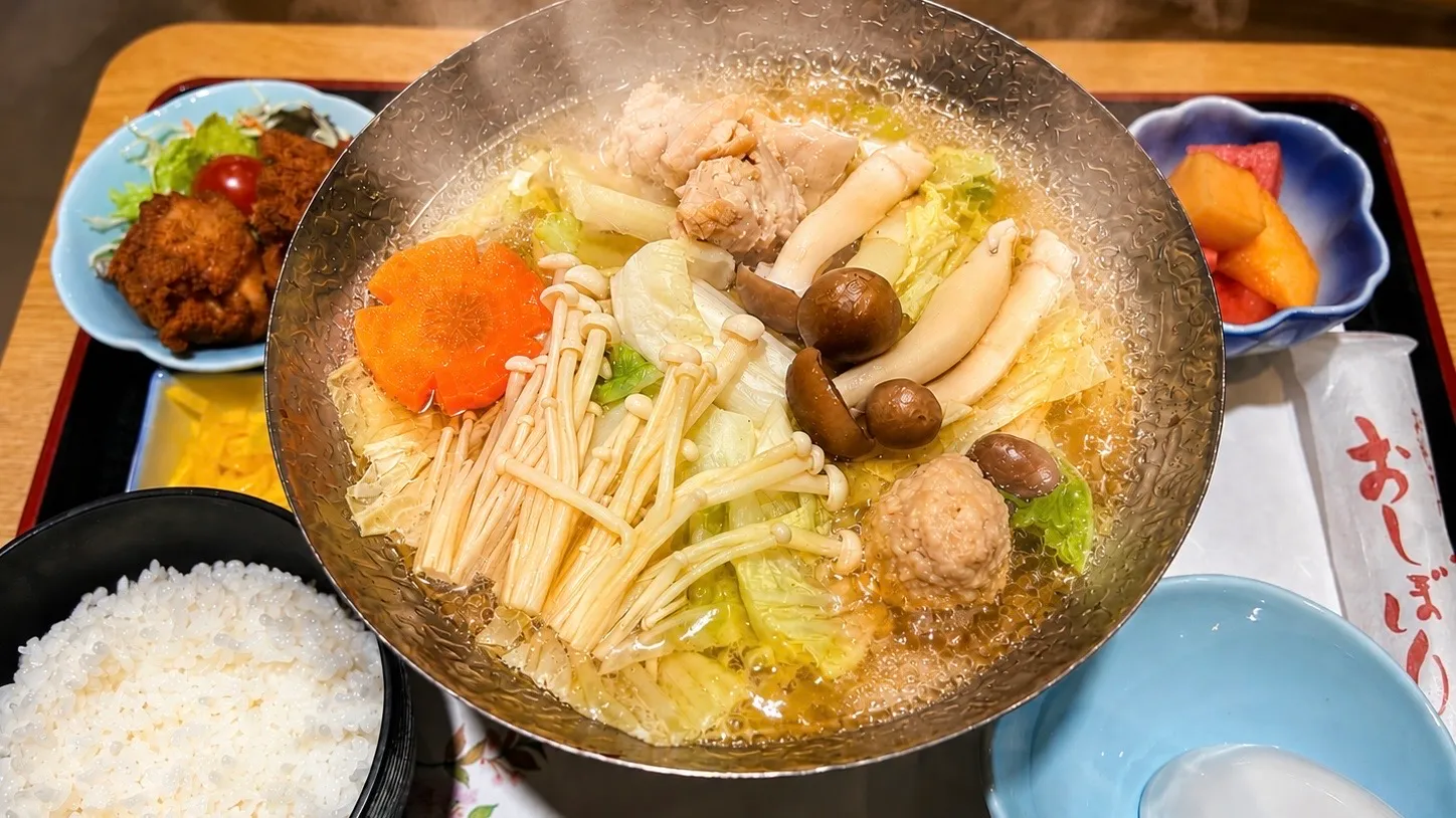 具材がたっぷり入ったちゃんこ鍋とご飯、揚げ物、漬物、果物のセット