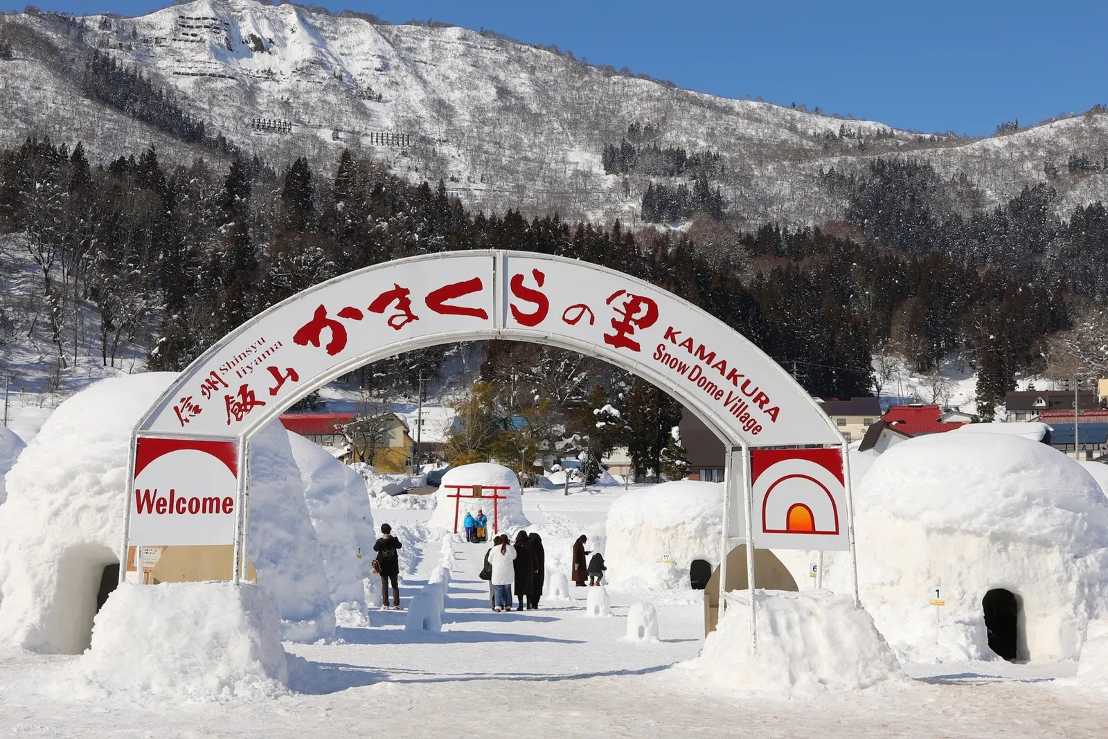 雪山を背景にした飯山かまくらの里の入口と雪のかまくら
