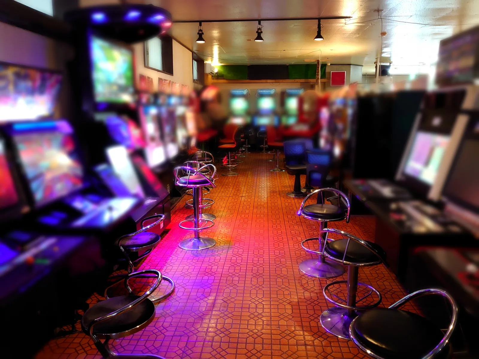 Inside a game arcade, with game cabinets and chairs lined up on both sides of the aisle