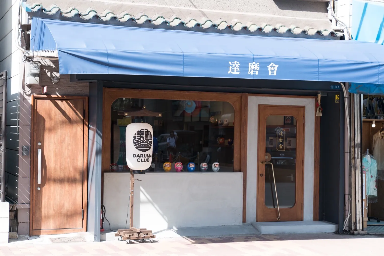 青いひさしに「達磨會」と書かれた店舗外観と店名入りの提灯