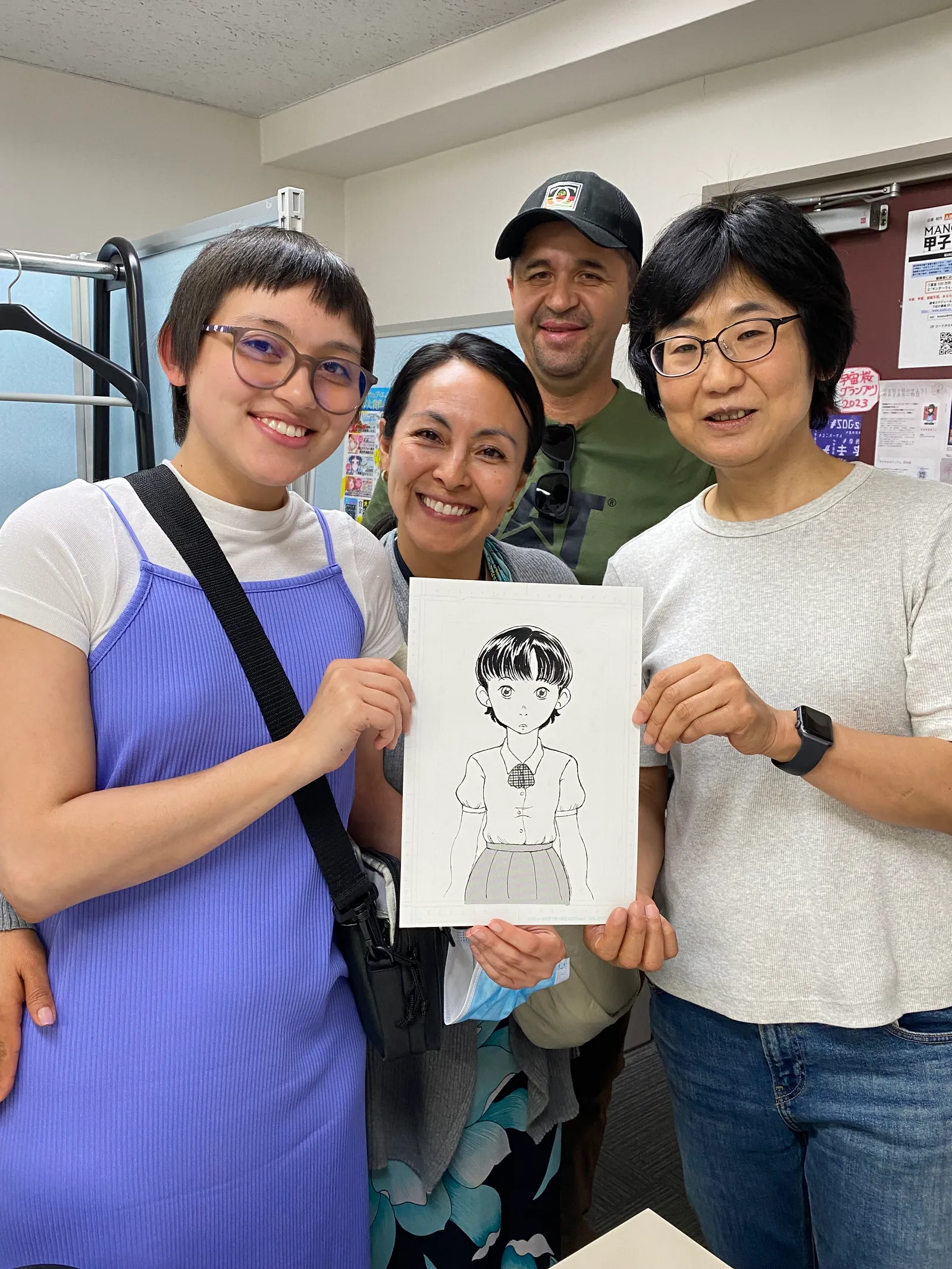 A photo of an instructor and participants holding up a finished manga page of a girl