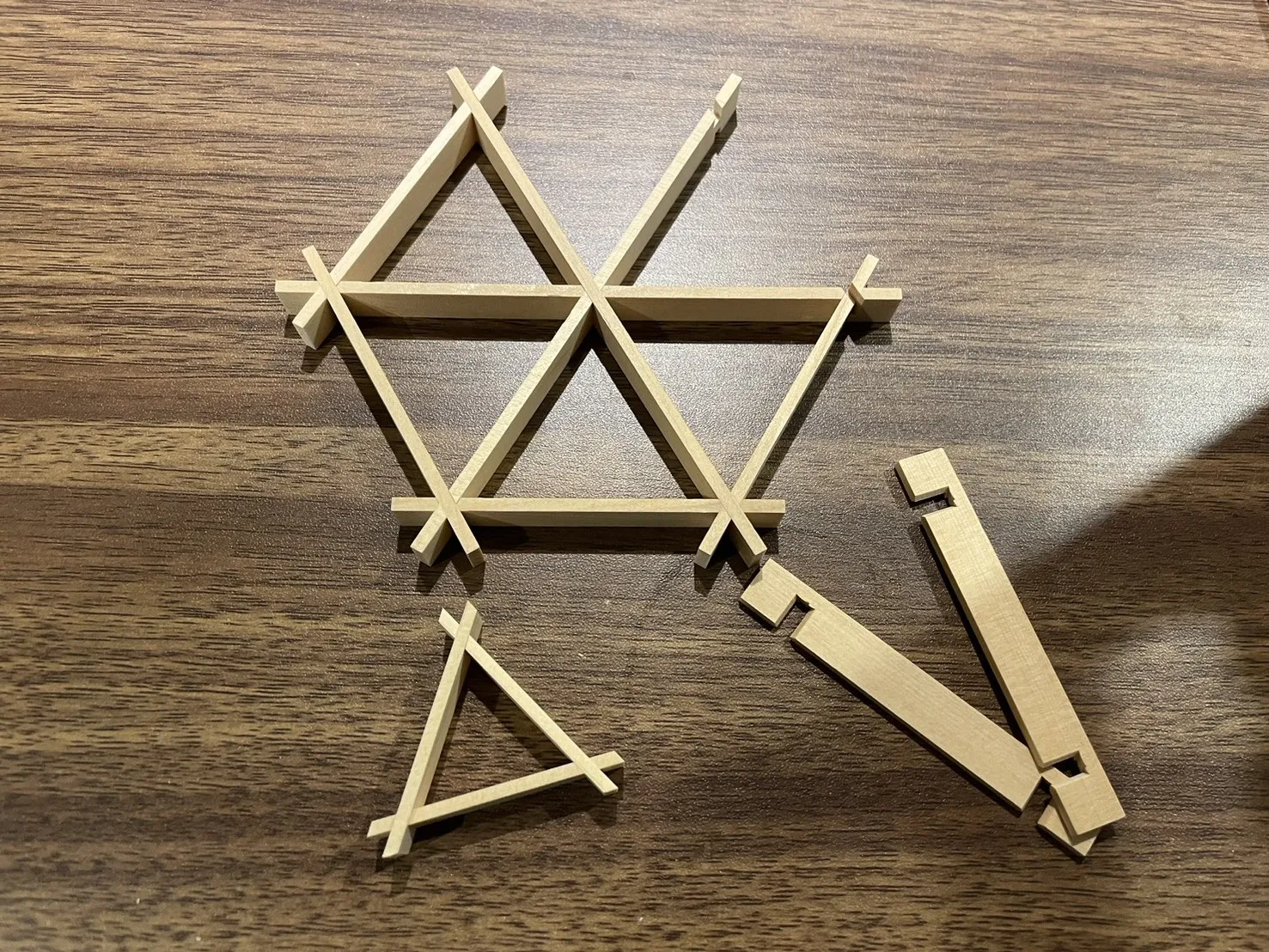 Kumiko parts assembled into a triangle on a wooden table, next to unused thin strips of wood