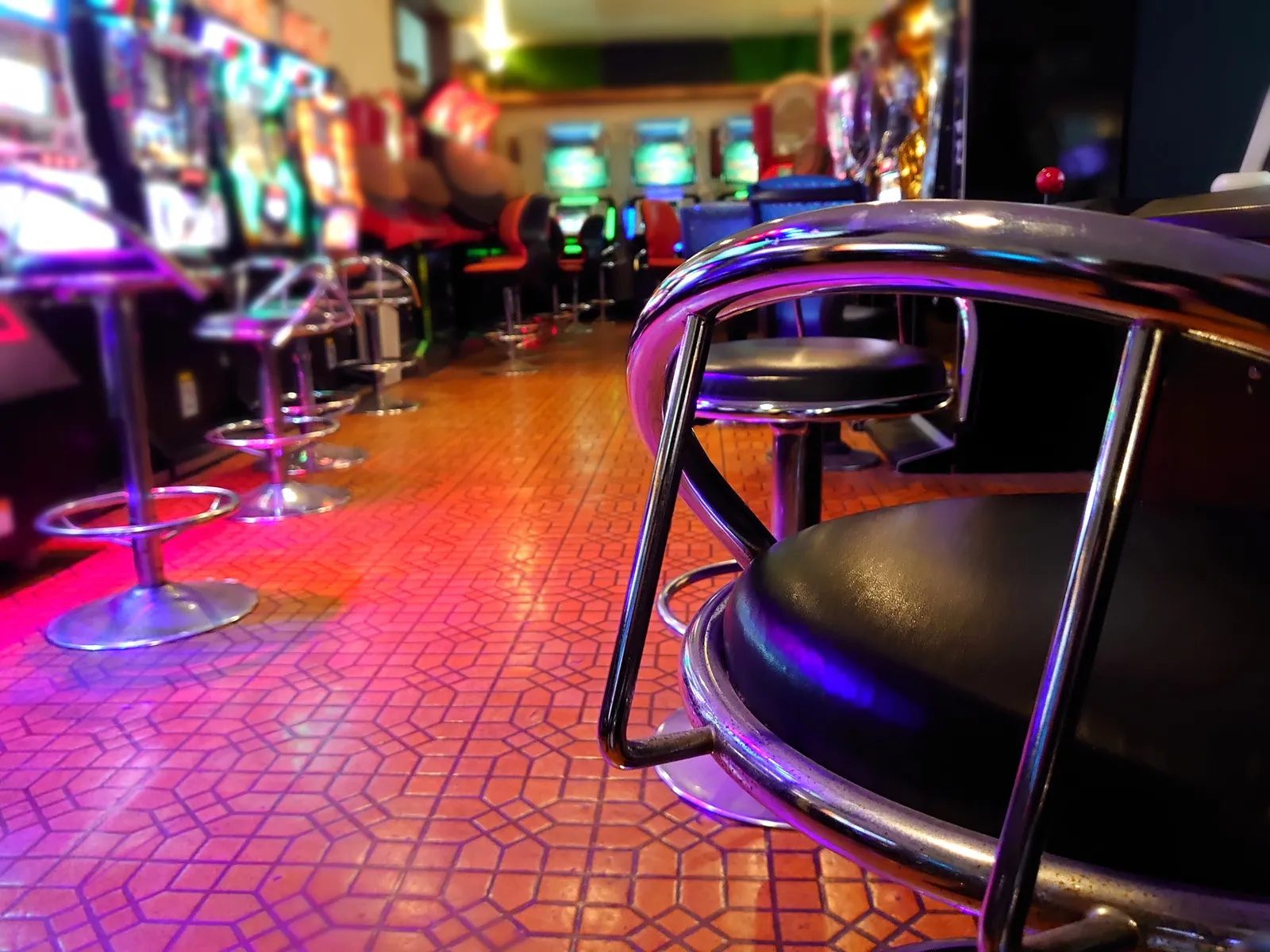 Chairs lined up in front of game cabinets, with the glow of the screens lighting the arcade