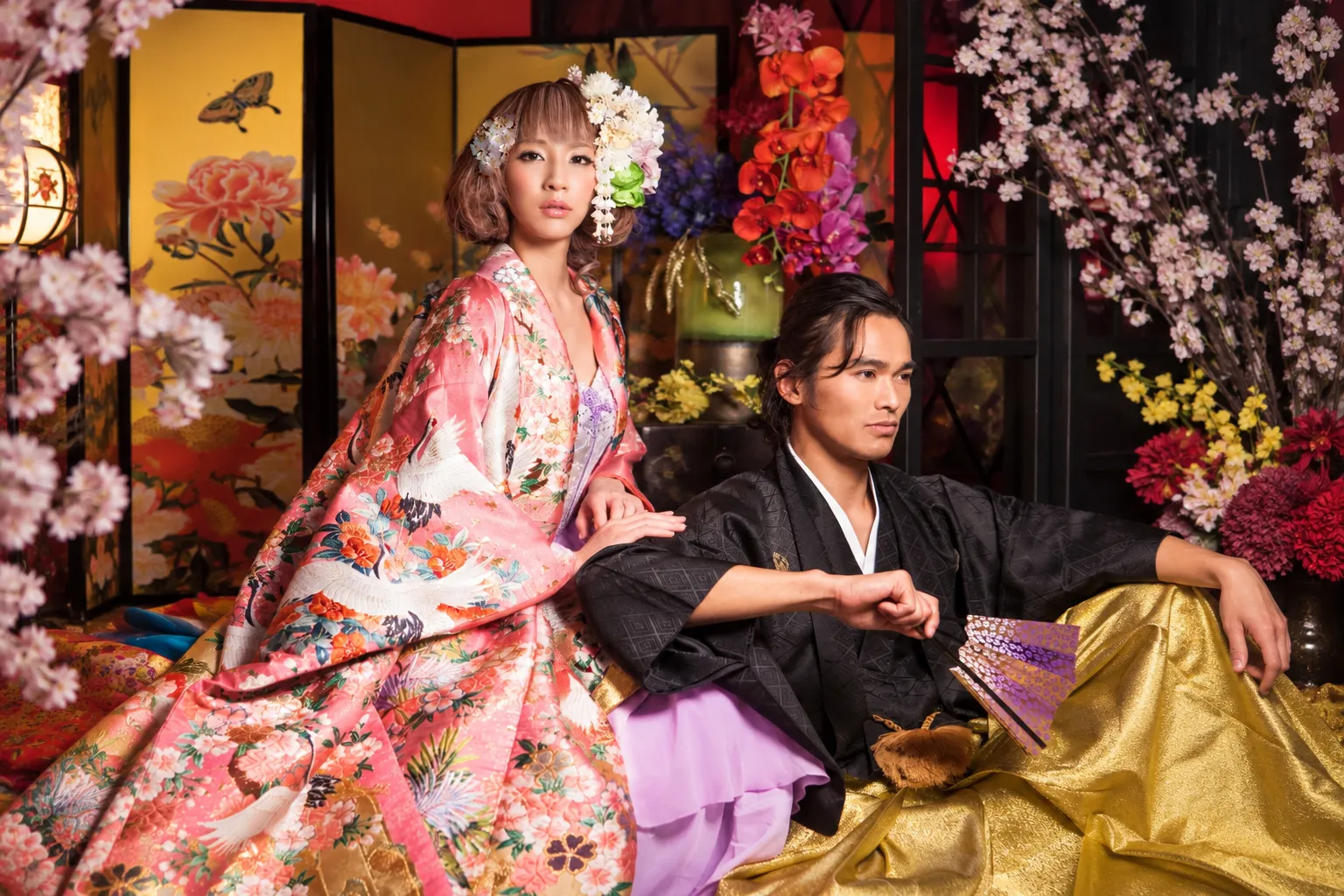 金屏風と桜を背景に、ピンクの打掛の女性と黒い和装の男性が座る