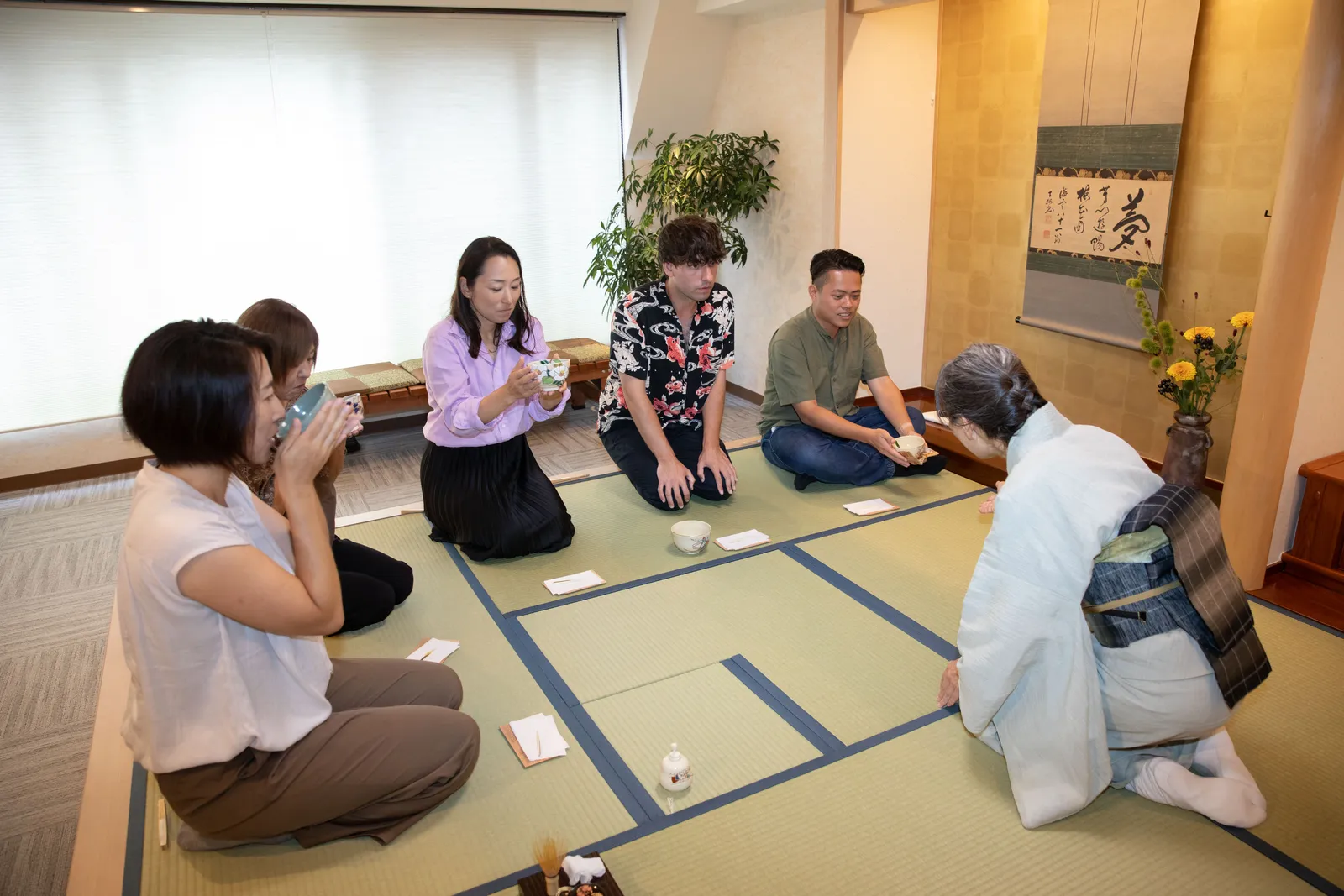 畳に並んで座り茶碗で抹茶を飲む参加者と講師