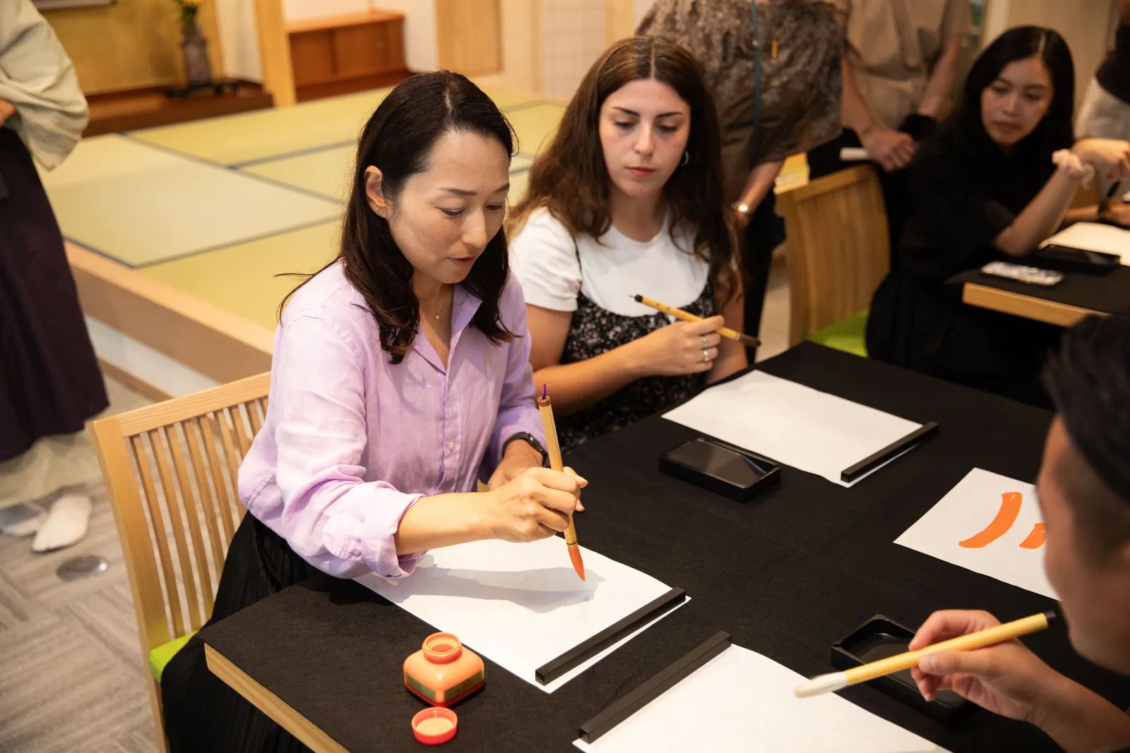 An instructor writing a model character in red ink next to a participant