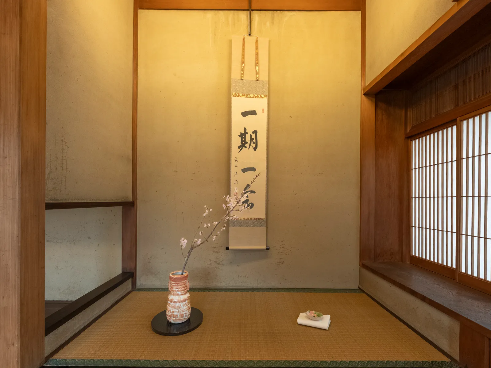 A Japanese-style room with a scroll reading "ichi-go ichi-e" and a flower arrangement in the tokonoma alcove