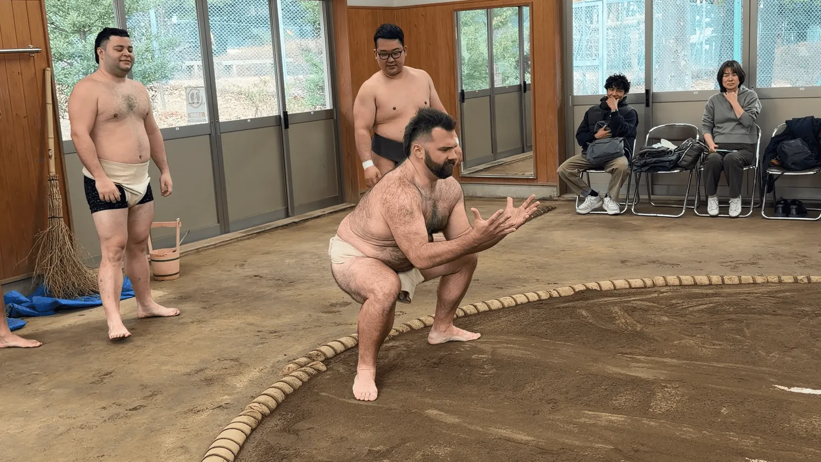 A participant crouching low while a rikishi watches on