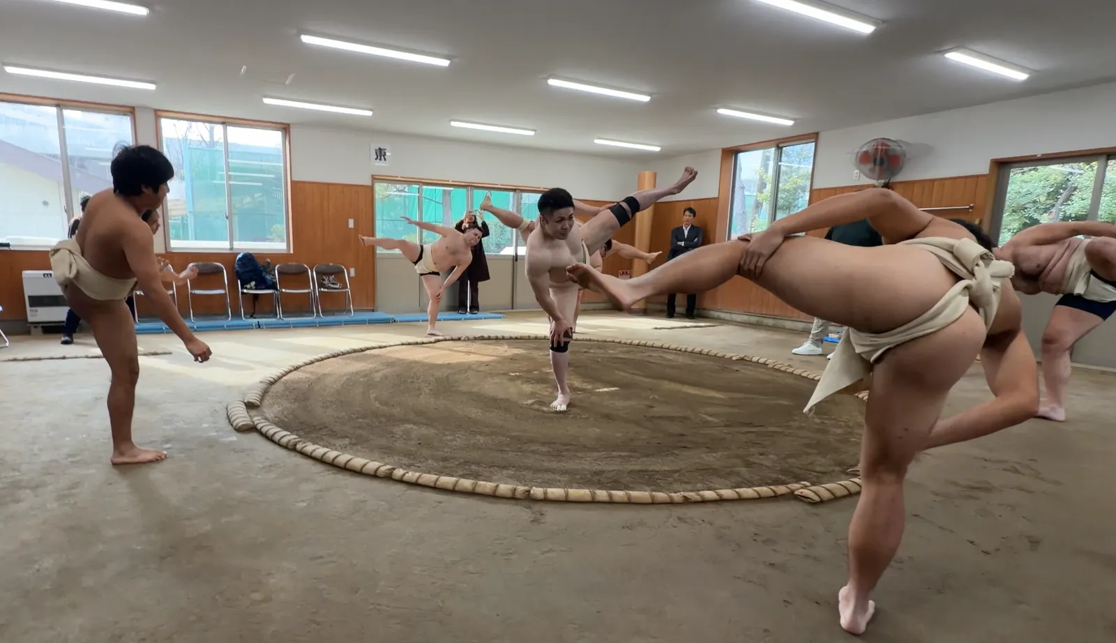 The rikishi and a participant raising one leg high in the spacious training hall