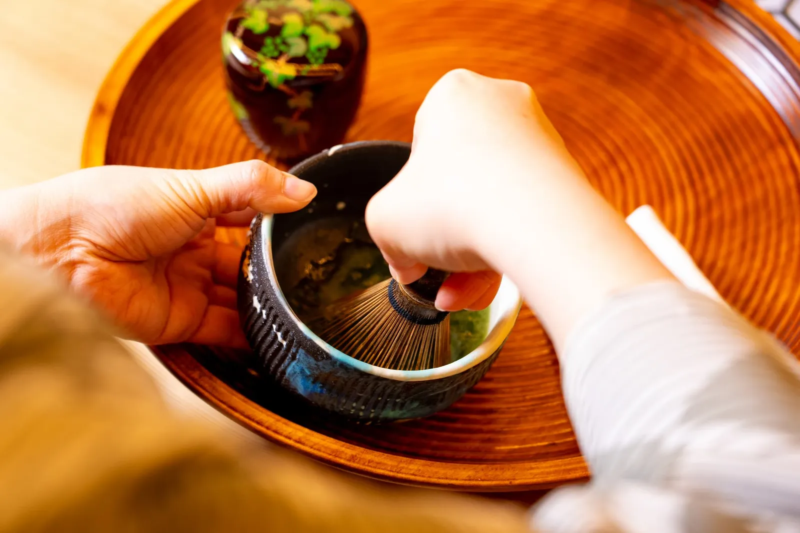 木の盆に置かれた茶碗を押さえながら茶筅を振る手元