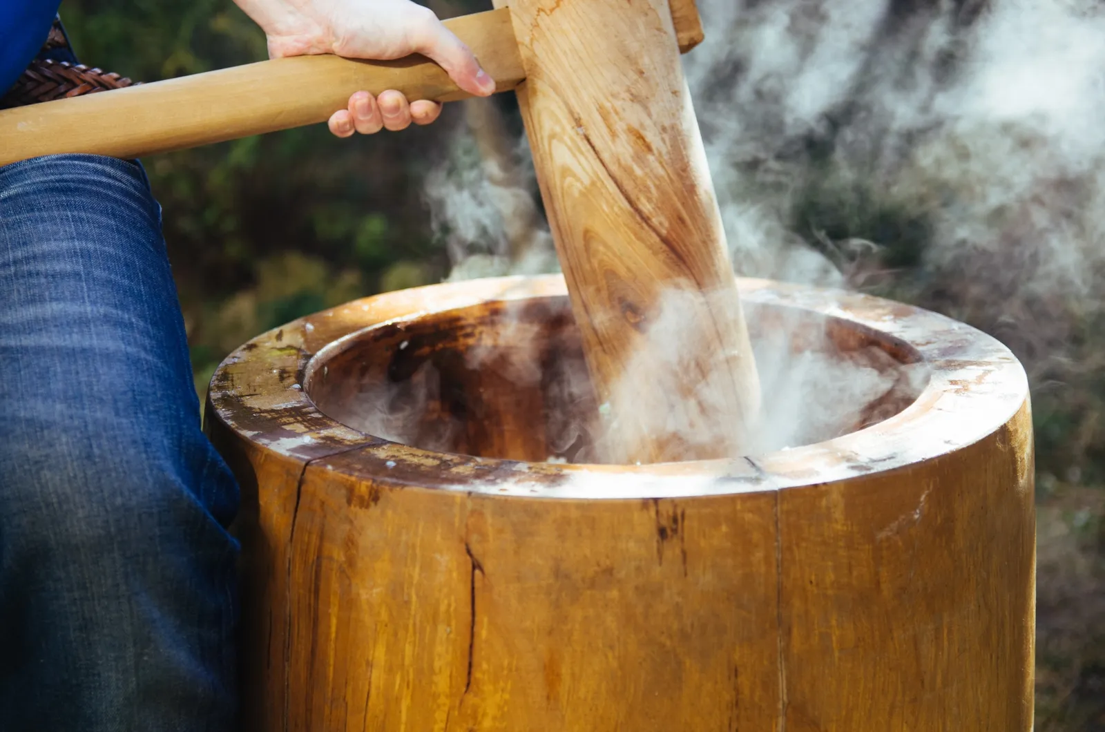 湯気の立つ臼に杵を入れ、餅をついている手元
