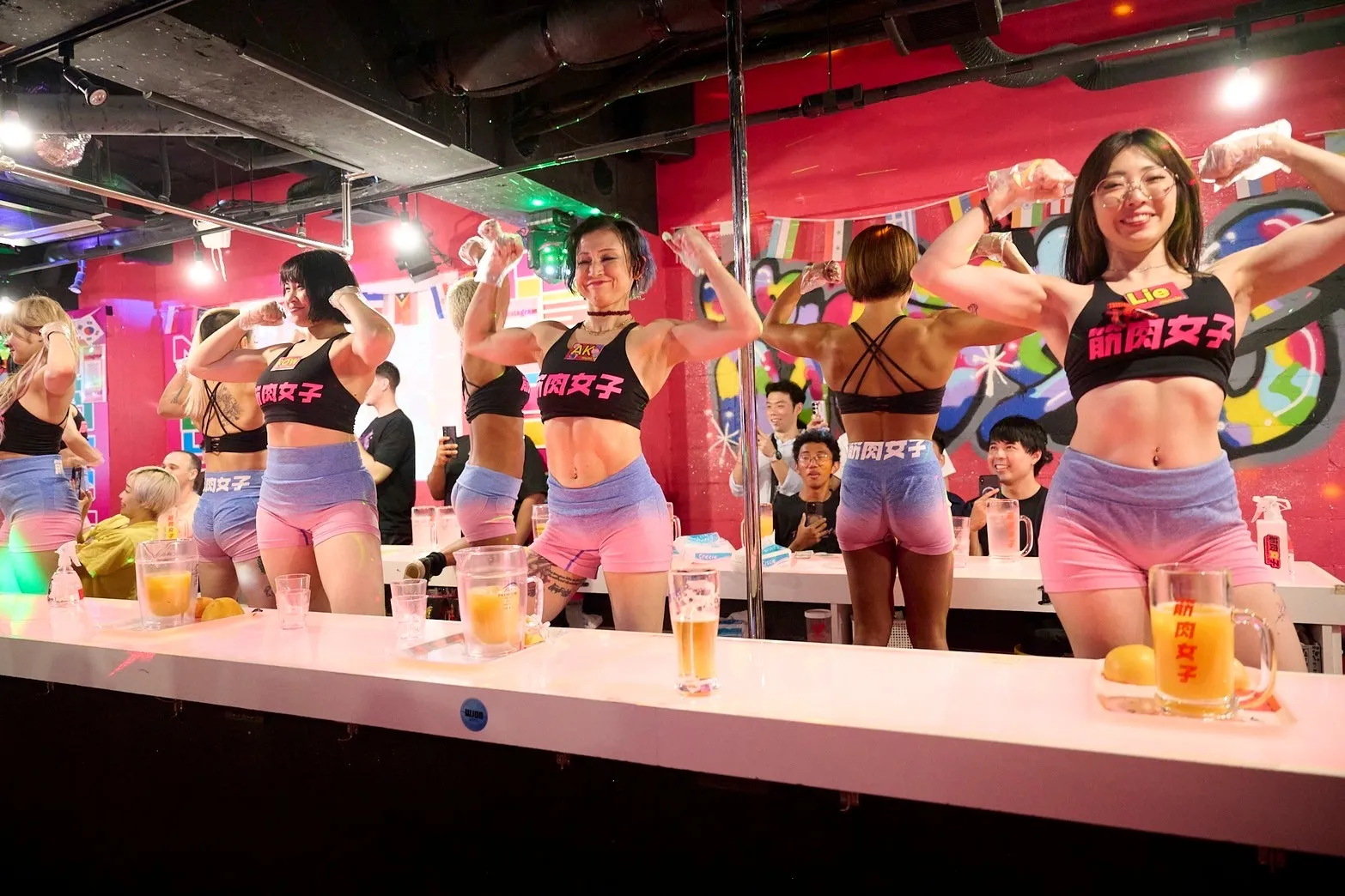 Members flexing their biceps behind pitchers and mugs lined up on the counter