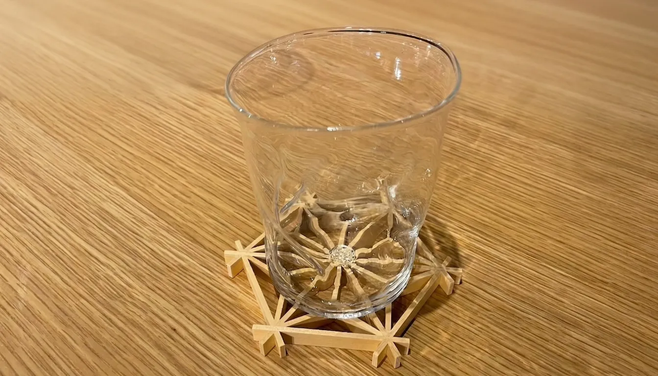 An asanoha kumiko coaster on a wooden table with a glass on top