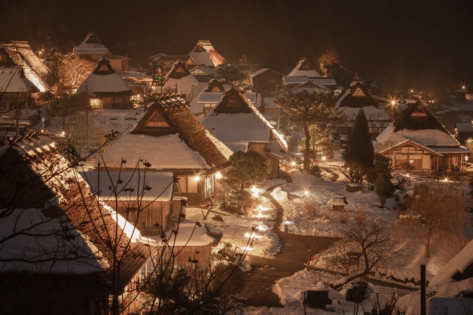 暖かな灯りに照らされた雪の茅葺き集落