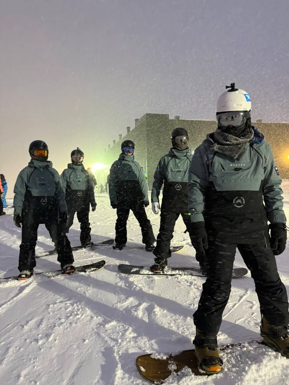 A group standing in evening light on the slopes, donning snowboards