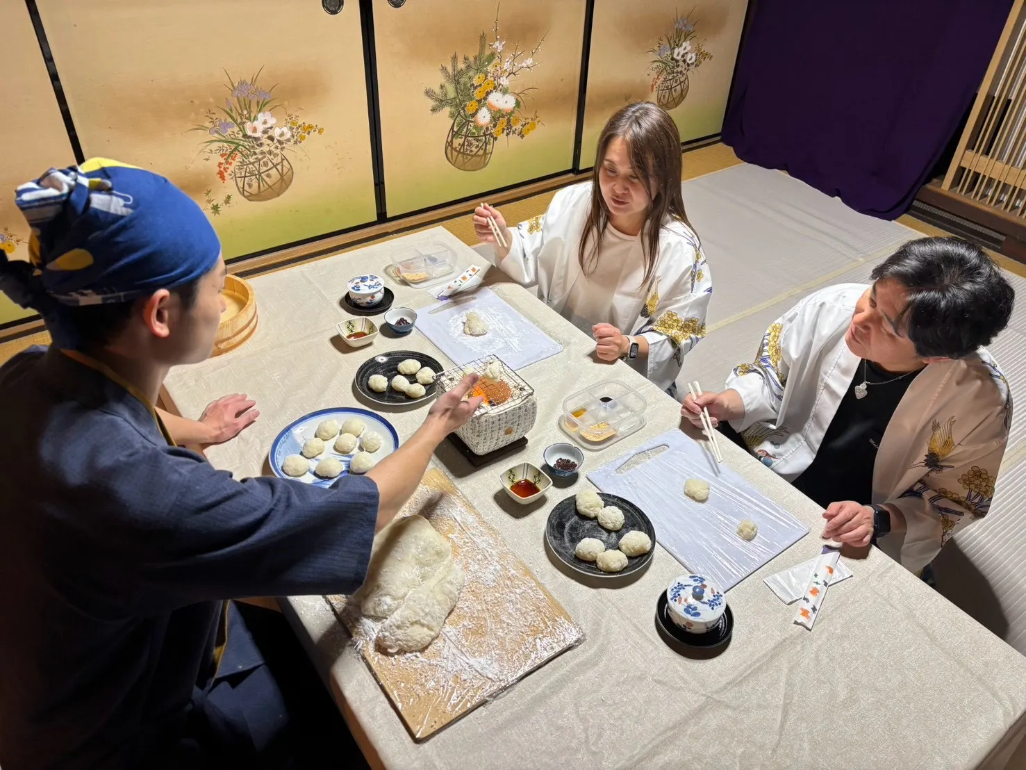 座敷のテーブルで職人が餅を伸ばし、参加者が七輪で餅を焼く様子