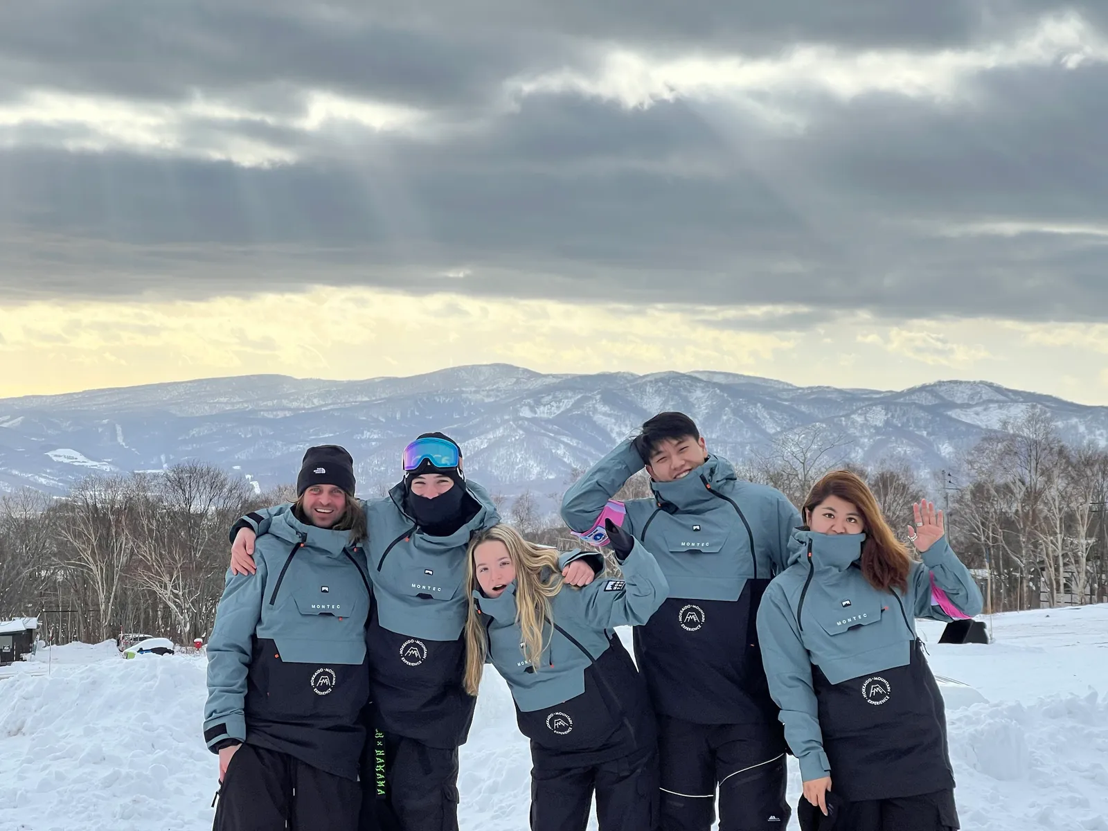 Five people in matching outfits standing in a line with Niseko mountains in the background