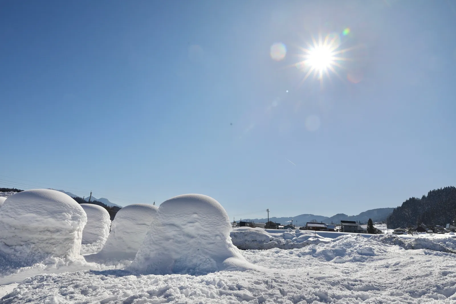 青空と太陽の下で雪原に並ぶ飯山のかまくら