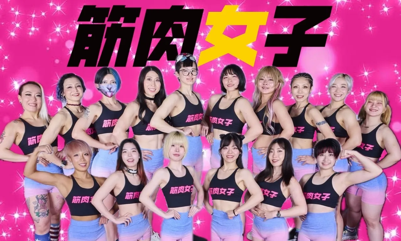 Members in uniform standing in front of the "筋肉女子" (Kinniku Joshi) sign