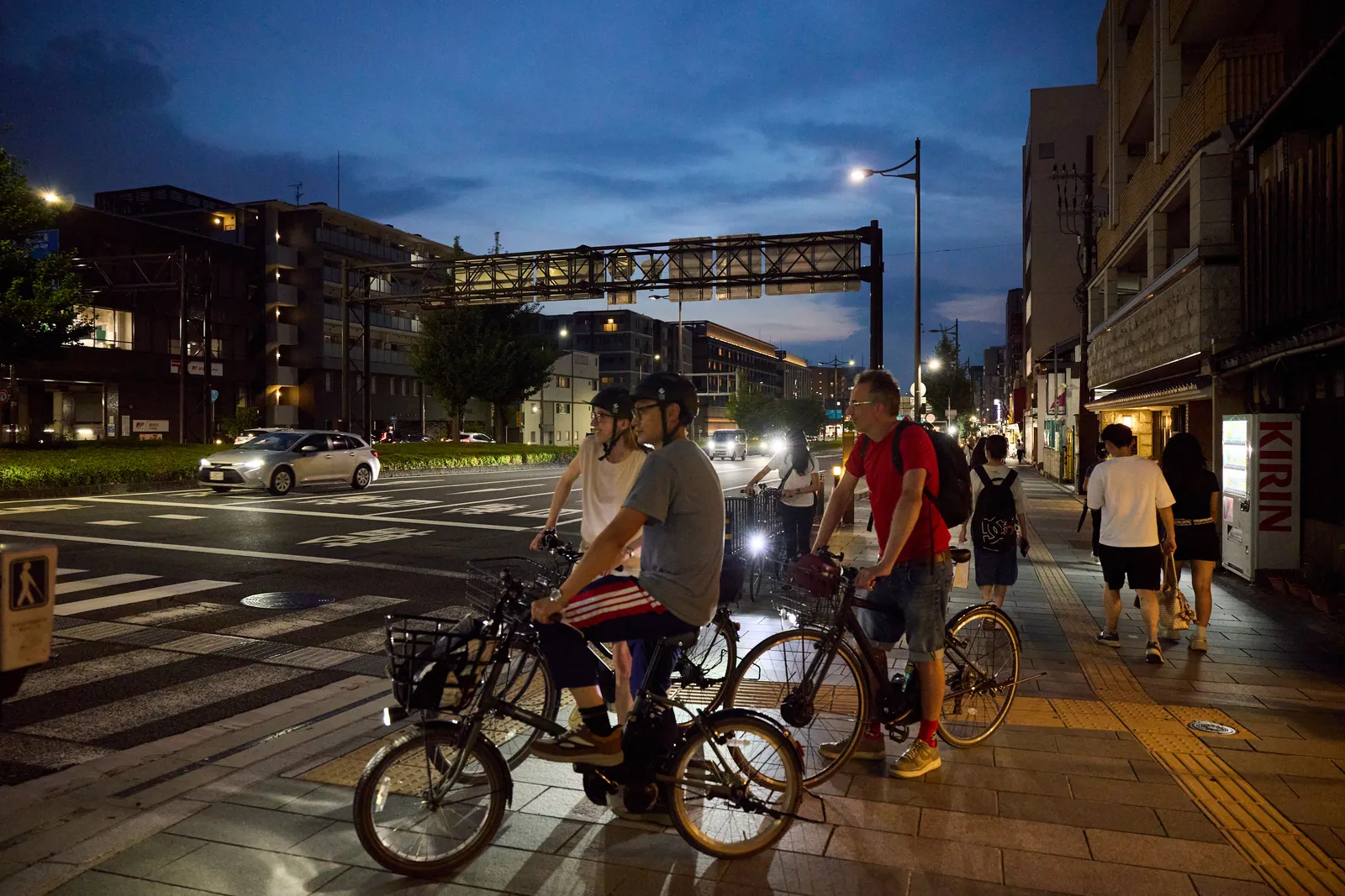 Participants on their bikes waiting at a traffic light along a main road at dusk