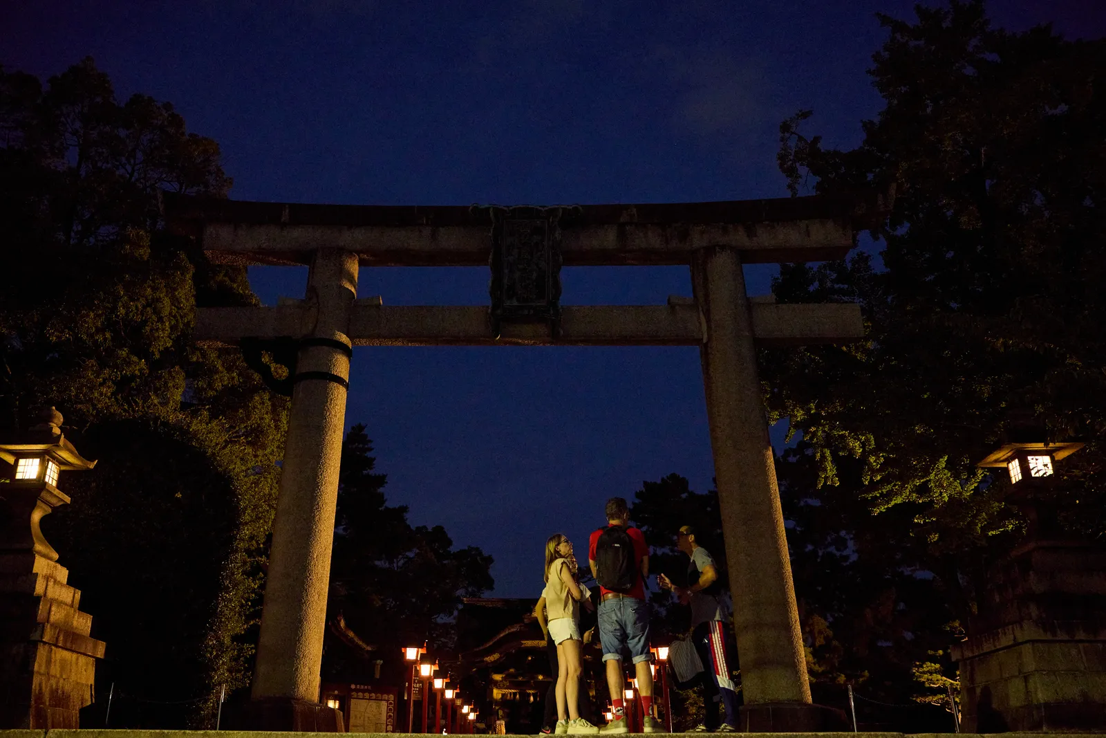 A participant and the guide standing under the stone torii gate of Toyokuni Shrine at night