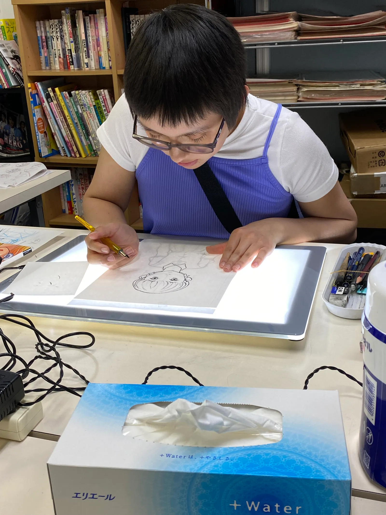 A participant placing paper on a light board and drawing a face with a dip pen