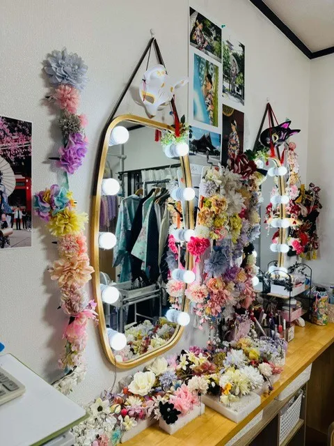 ライト付きの鏡の周りに造花のヘアアクセサリーが多数飾られた支度スペース