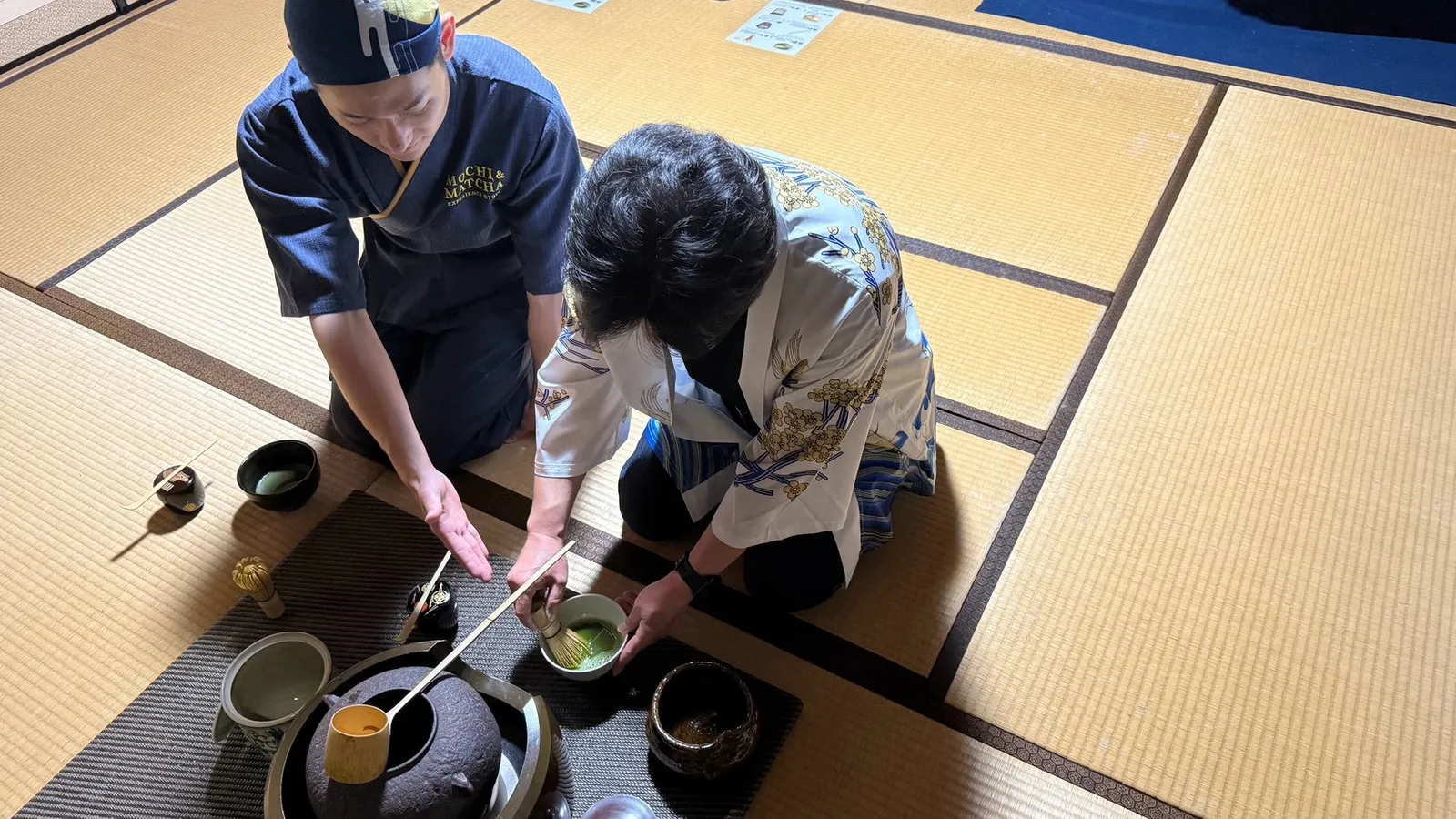 畳の上で講師が参加者に茶碗と茶筅の扱い方を指導する様子