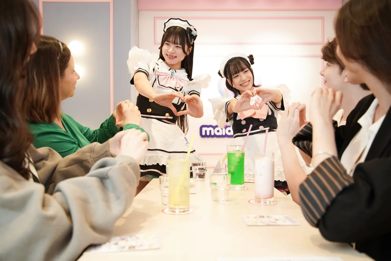 メイド2人がテーブル席の客とハートの仕草をそろえる店内の様子