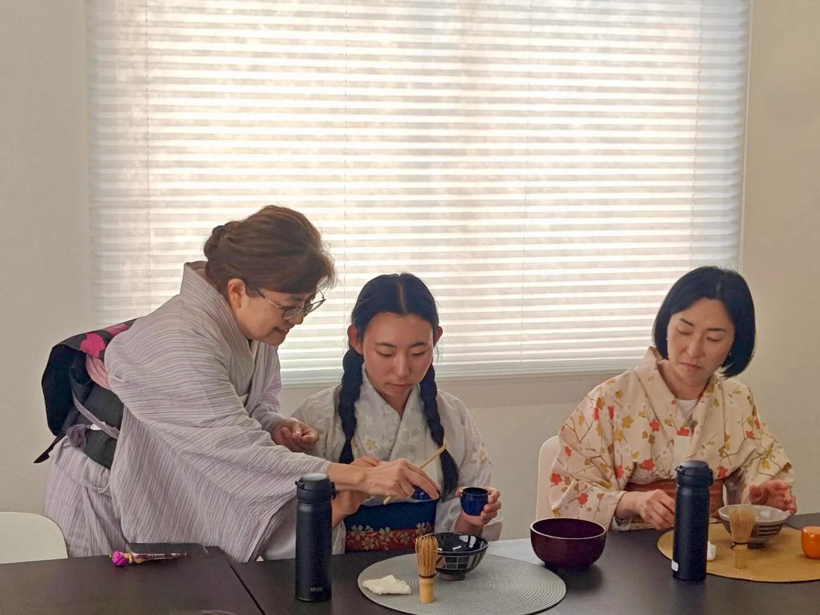 An instructor leaning in close to a participant, teaching how to handle the tea caddy and tea scoop