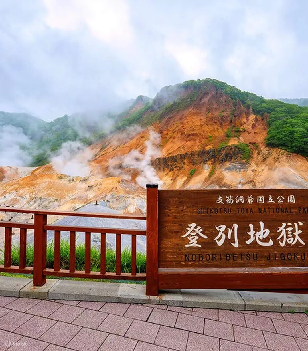 支笏洞爺国立公園と登別地獄谷の木製看板、奥に噴気の上がる谷