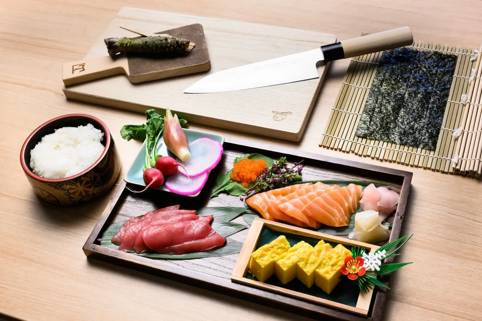 참치, 연어, 달걀말이, 초밥용 밥, 칼, 김발이 놓인 테이블