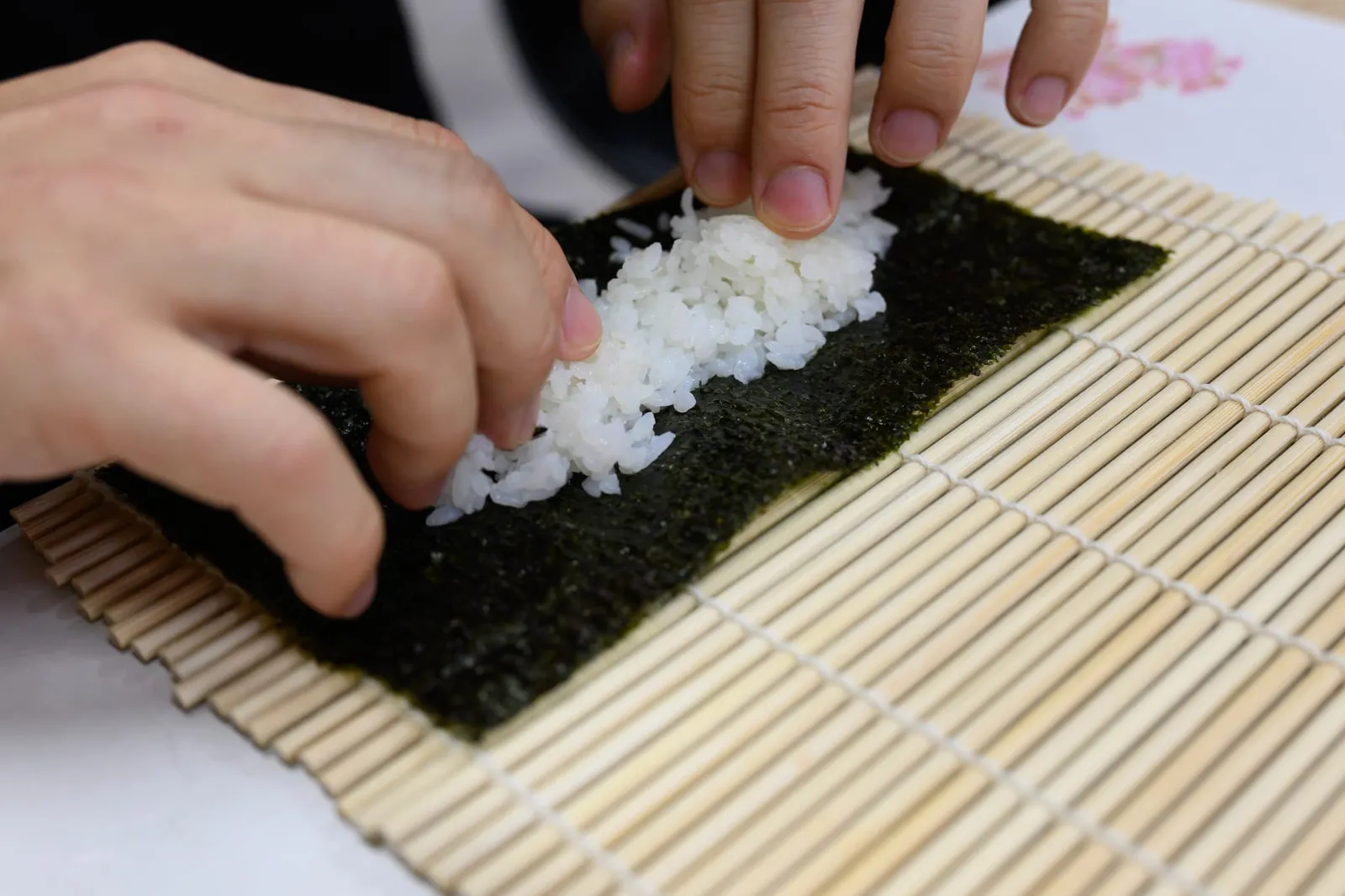 김발 위의 김에 초밥용 밥을 펼치는 손