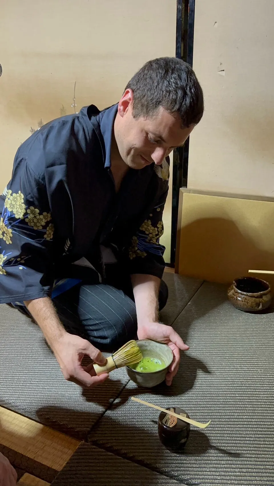 羽織姿の男性が茶碗を持ち茶筅で抹茶を点てる様子