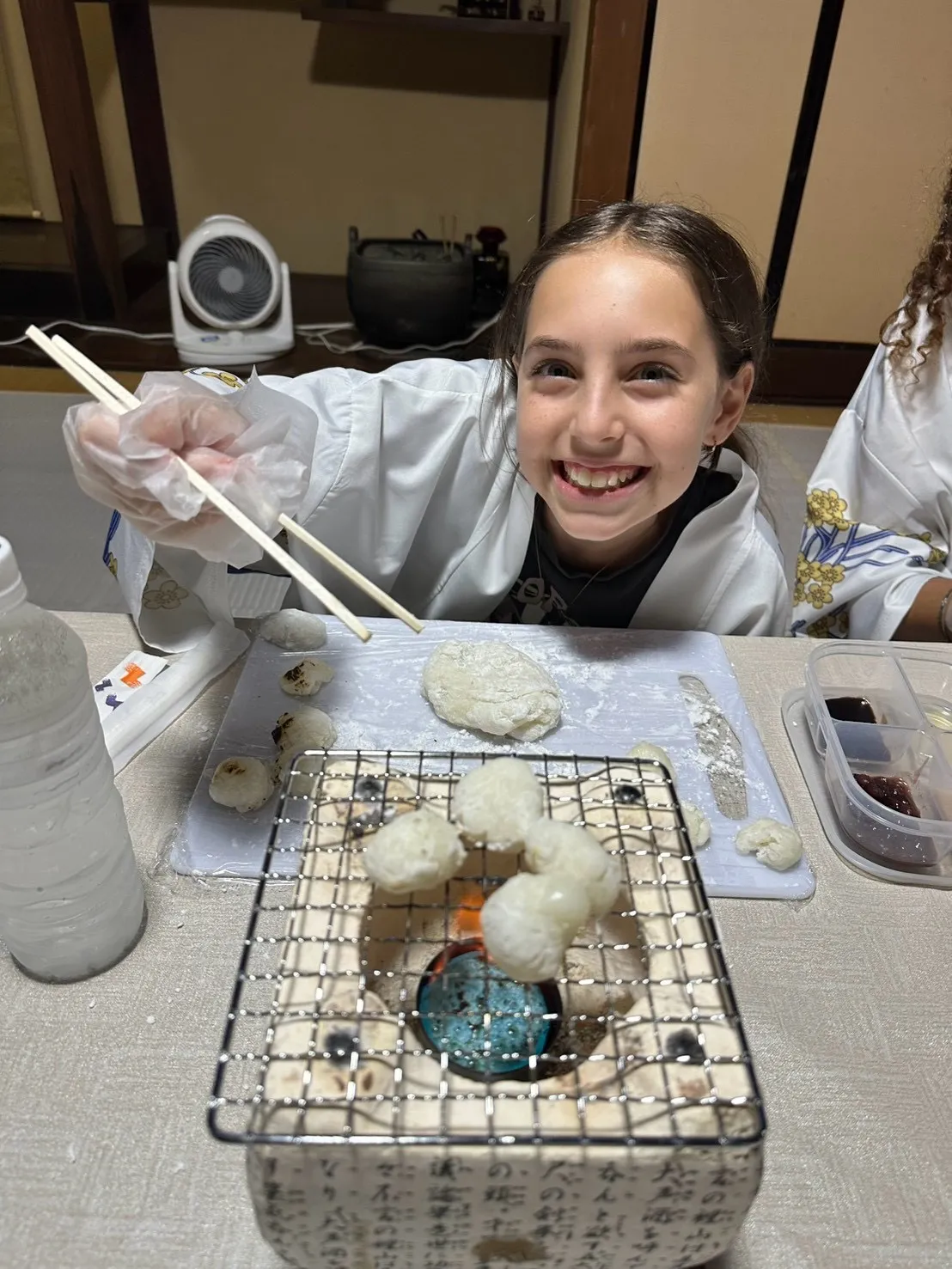 七輪の網の上で焼かれる複数の餅と箸を持つ参加者
