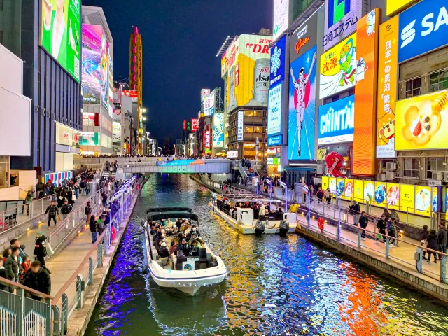 看板の光が川面に映り、遊覧船が進む夜の道頓堀