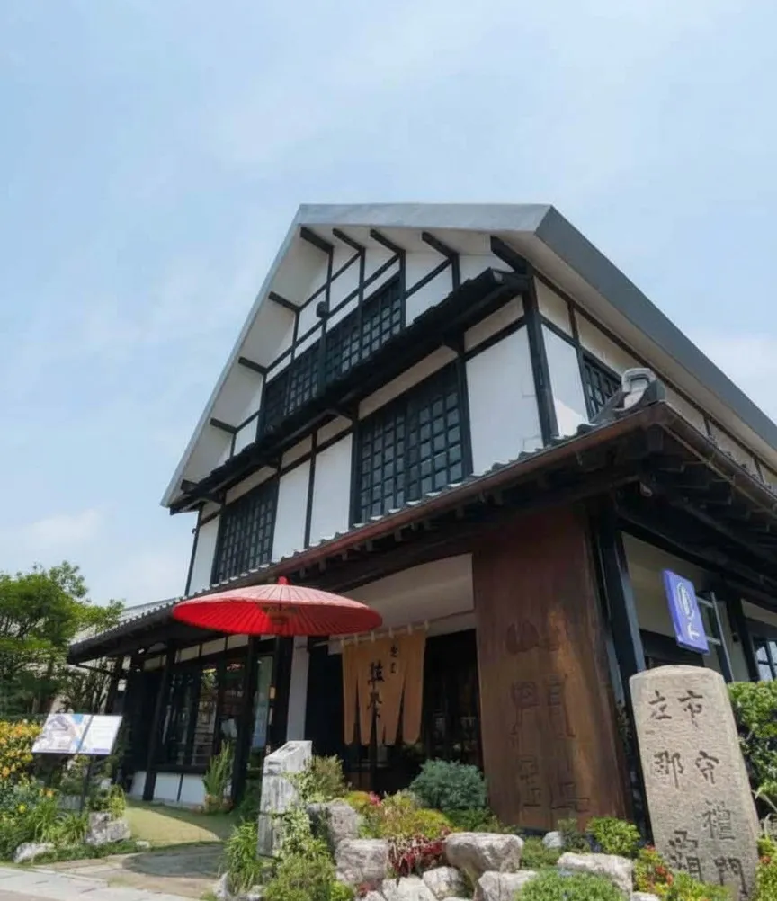 Exterior of the Shuri Ryusen building with white walls, black wood trim, and a red Japanese umbrella