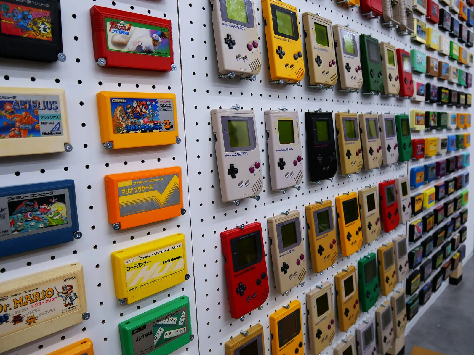 壁に整列して展示された初代ゲームボーイ本体とファミコンのカートリッジ