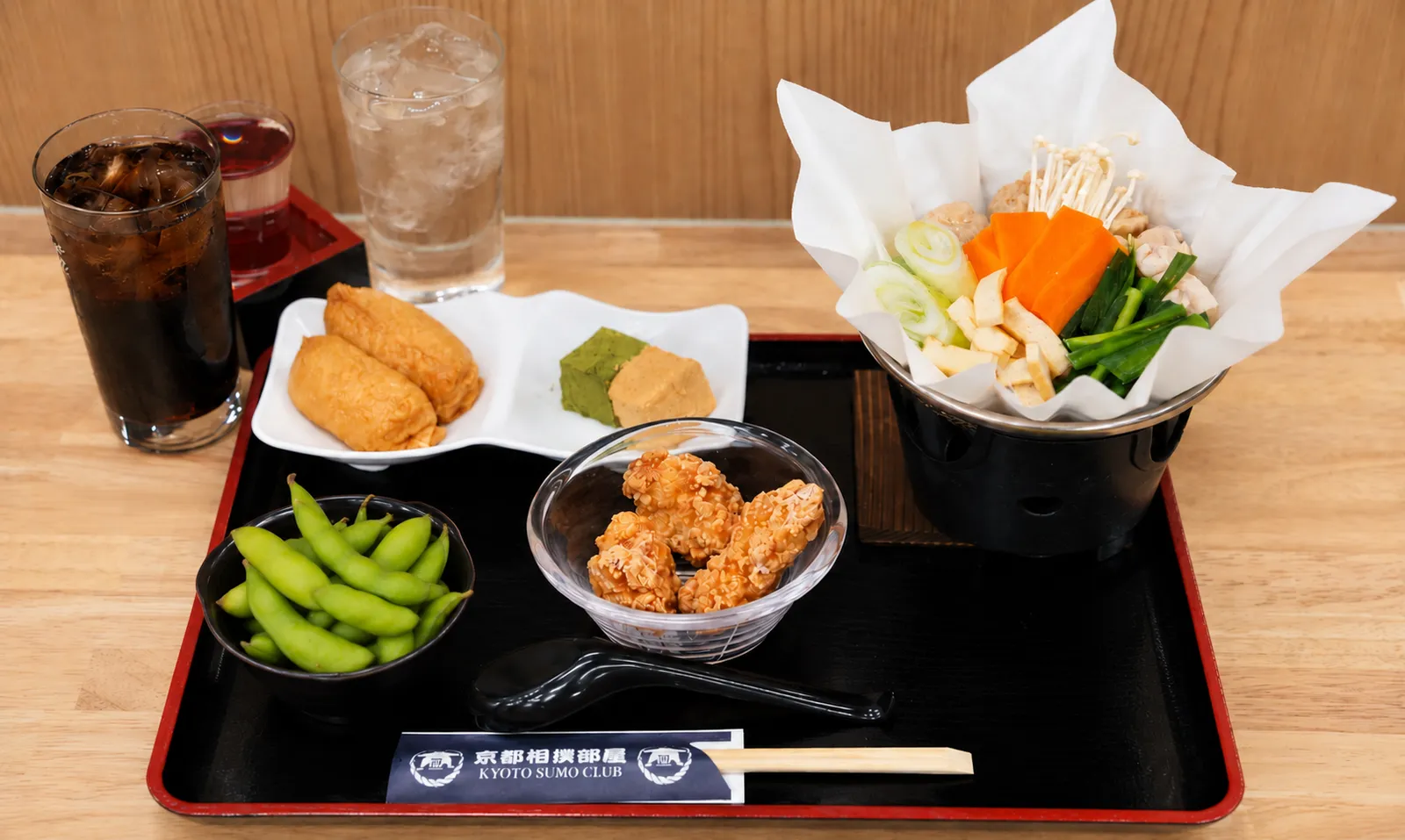 A tray with chicken chanko nabe, inari sushi, fried chicken, edamame, and drinks