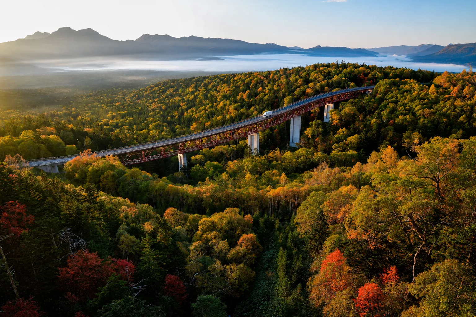 紅葉の森を渡る赤い橋と朝霧の山並み