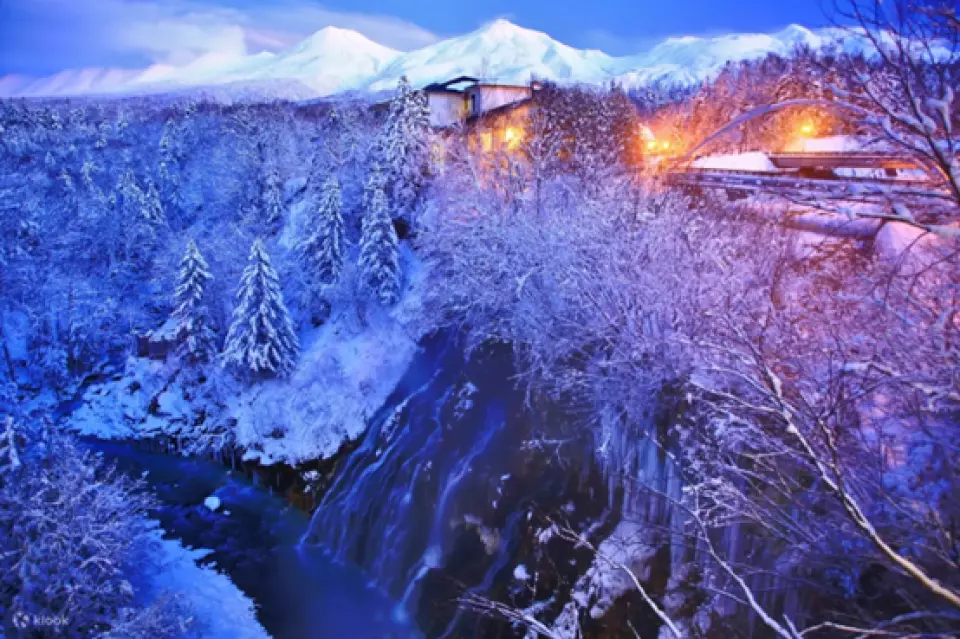 A snowy gorge and waterfall lit by the evening light, with snowy mountains behind