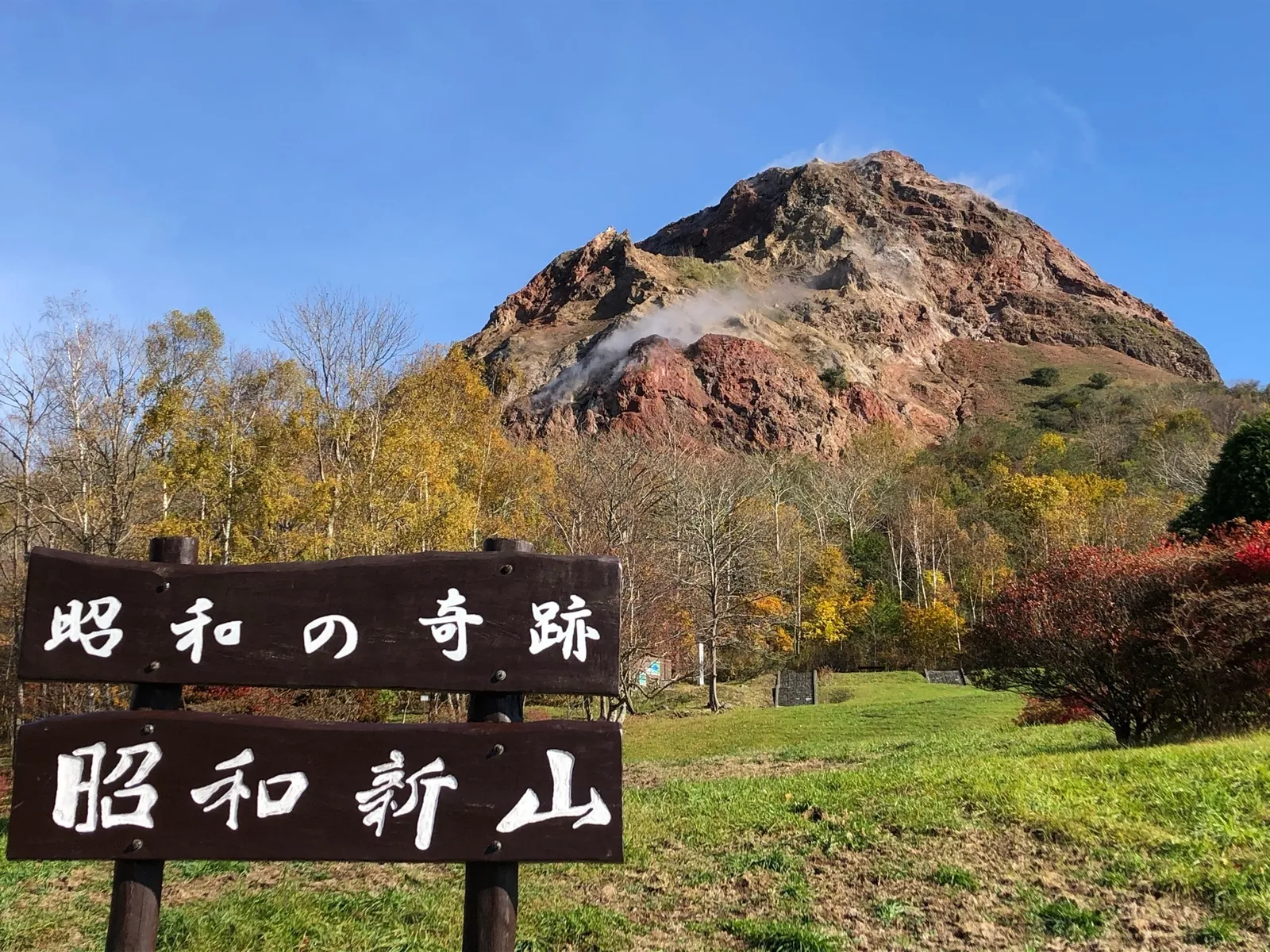 분기가 피어오르는 쇼와신잔의 붉은 갈색 산비탈과 '昭和新山' 표지판